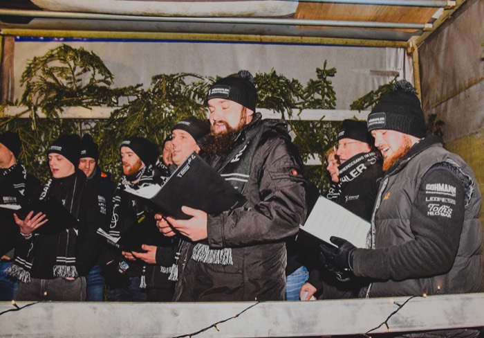 Nahaufnahme des Chores beim Singen, alle in dunklen Jacken mit Vereinsschals und Mützen.
