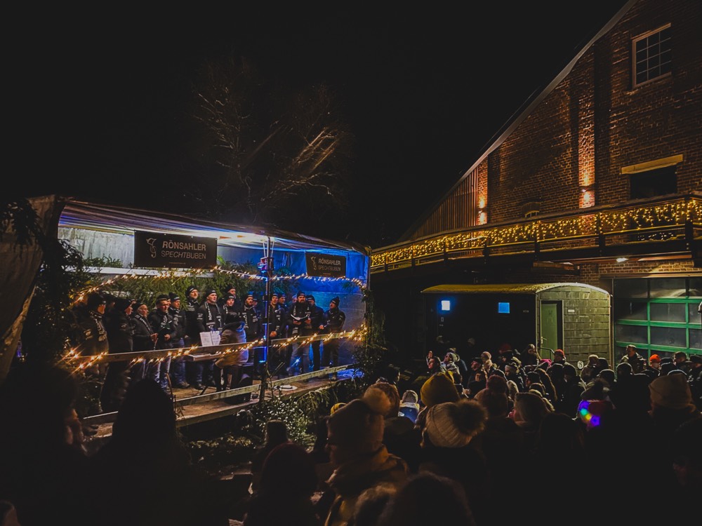 Abendlicher Auftritt beim Rönsahler Weihnachtsmarkt vor der Historischen Brennerei, Lichterketten und volles Publikum.